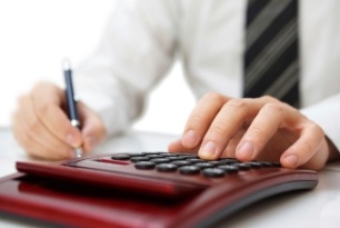 A person in a dress shirt and striped tie uses a calculator with one hand while holding a pen in the other, suggesting they are working on financial or accounting tasks.