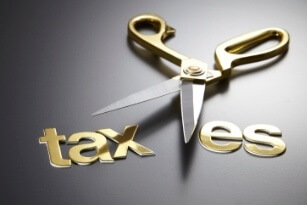 A pair of gold scissors is cutting through the word taxes, separating tax from es, symbolizing a tax cut or reduction.