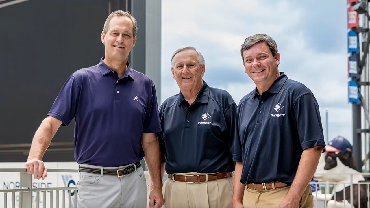 Padgett CEO Jeff Phillips and President Roger Harris stand with Atlanta Braves President and CEO Derek Schiller on a sunny day at Truist Park