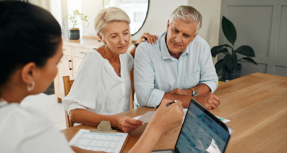 An older couple sit at a table looking over paperwork with a young accountant.