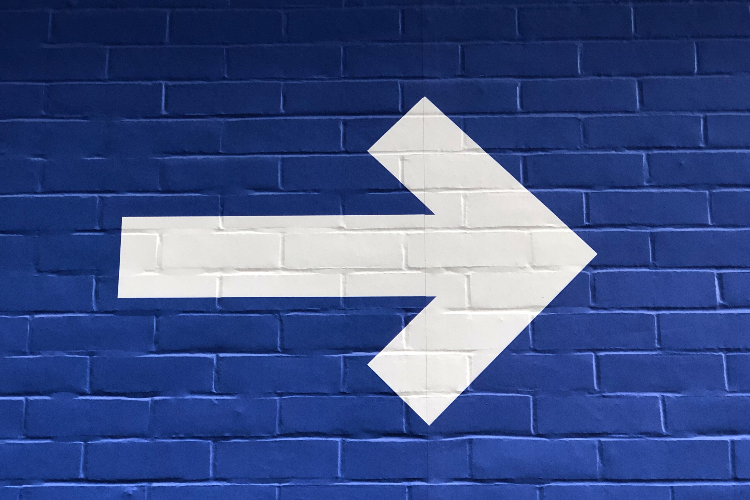 A large white right-pointing arrow, symbolizing AI-driven direction, is painted on a blue brick wall.