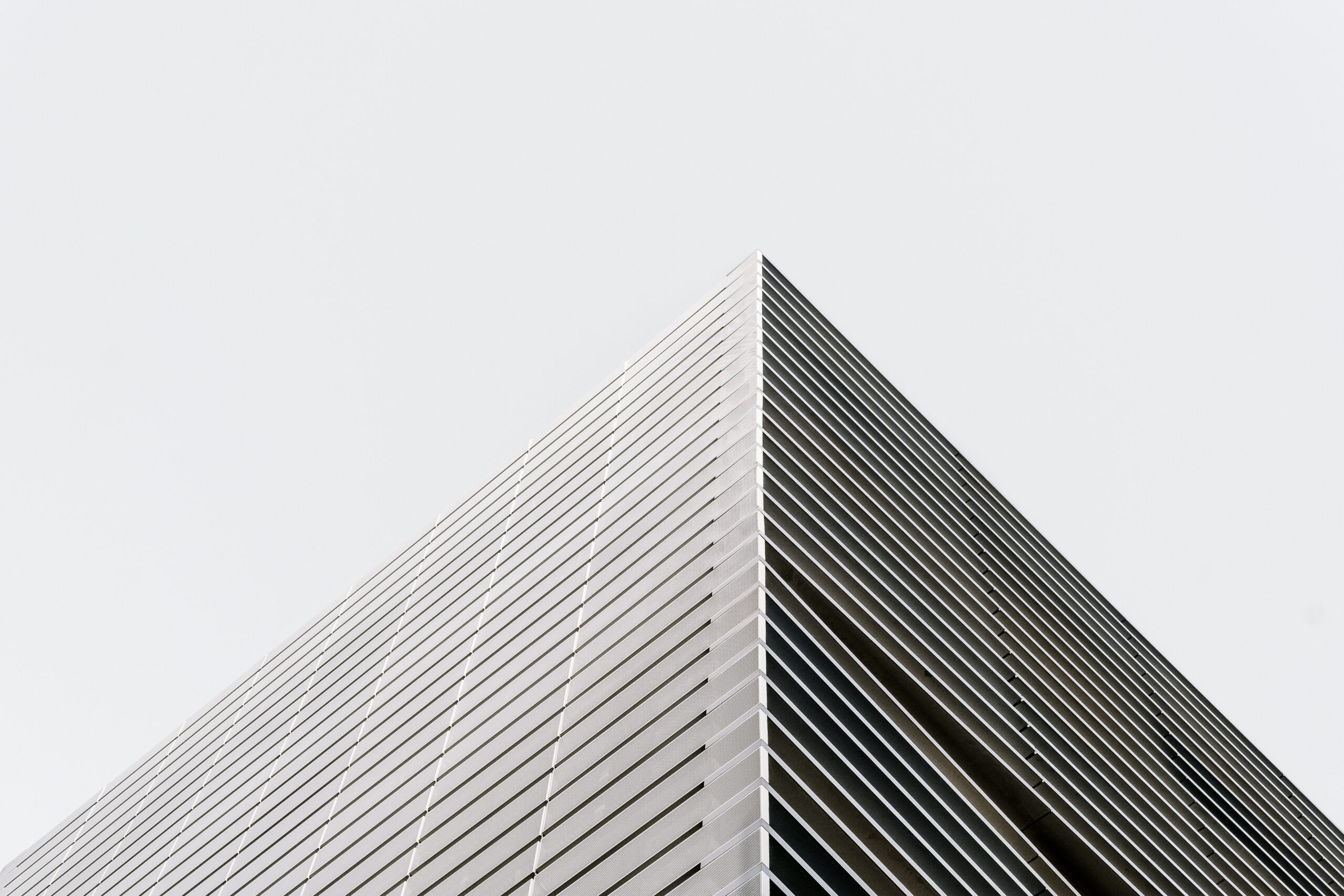 The photo shows the sharp corner of a modern building with horizontal metal lines on its facade, set against a pale, overcast sky—a striking image that echoes the clarity and structure found in architectural literacy.
