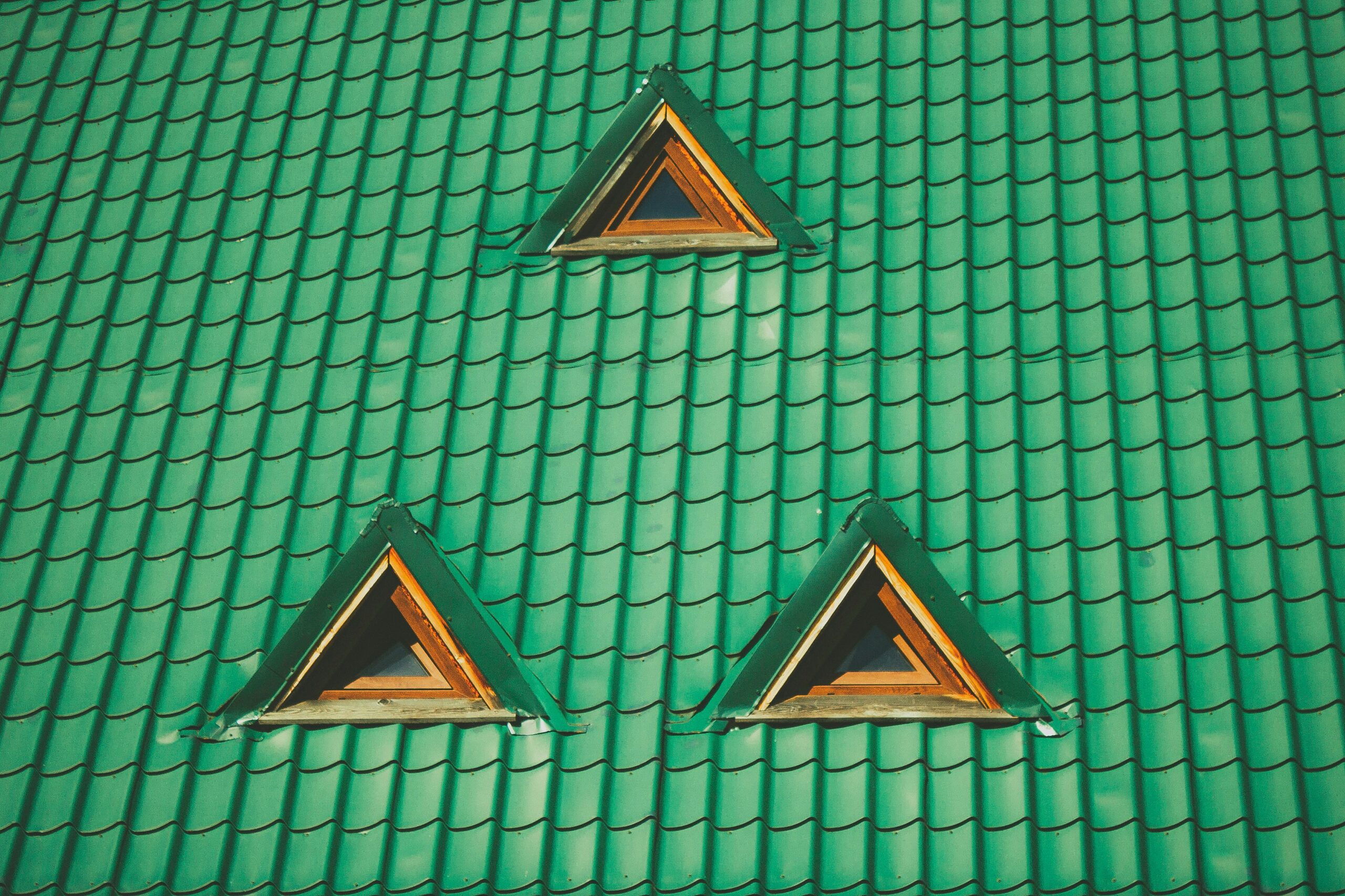 A green tiled roof with three triangular dormer windows, each framed with wood. Two windows are at the bottom, side by side, and one is above them in the center.
