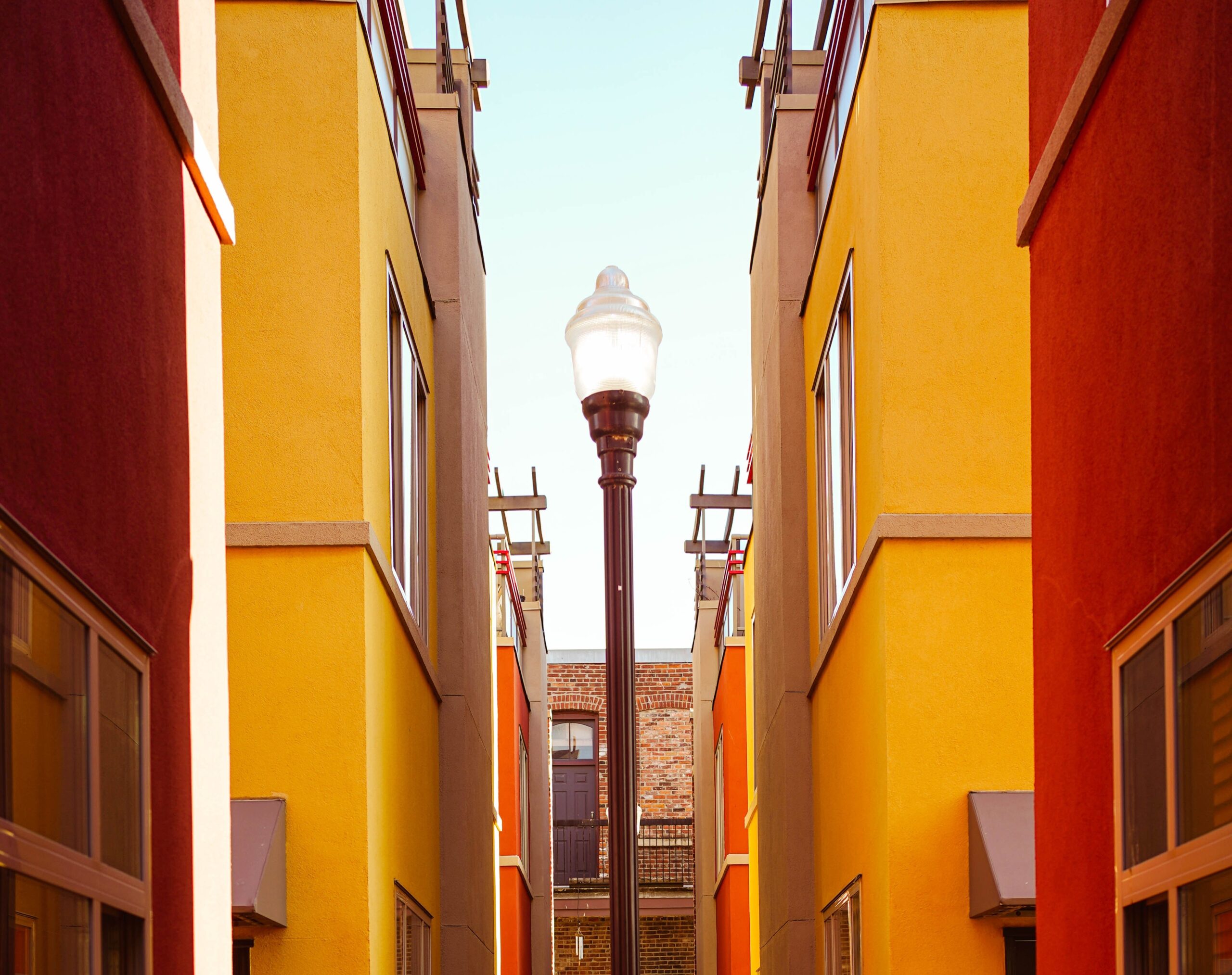 A streetlamp stands between two rows of colorful modern buildings with yellow and orange walls, under a clear sky—an unexpected calm distant from the bustle of city life and the worries of IRS deadlines.