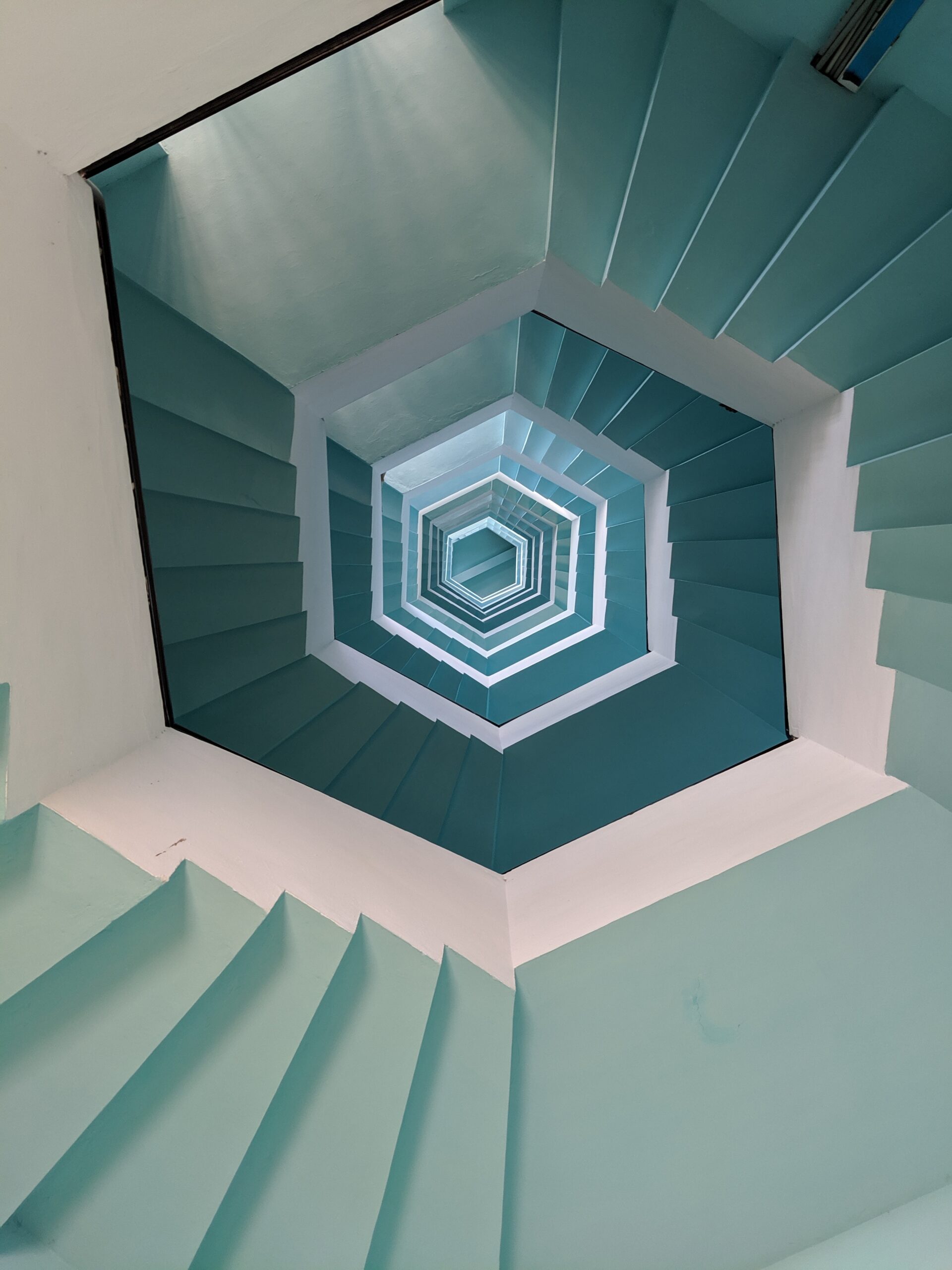 A view looking straight up a blue-tiled, hexagonal staircase, creating a geometric, symmetrical pattern that draws the eye toward the small hexagon of light at the top—resembling the orderly structure of an IRS flowchart.